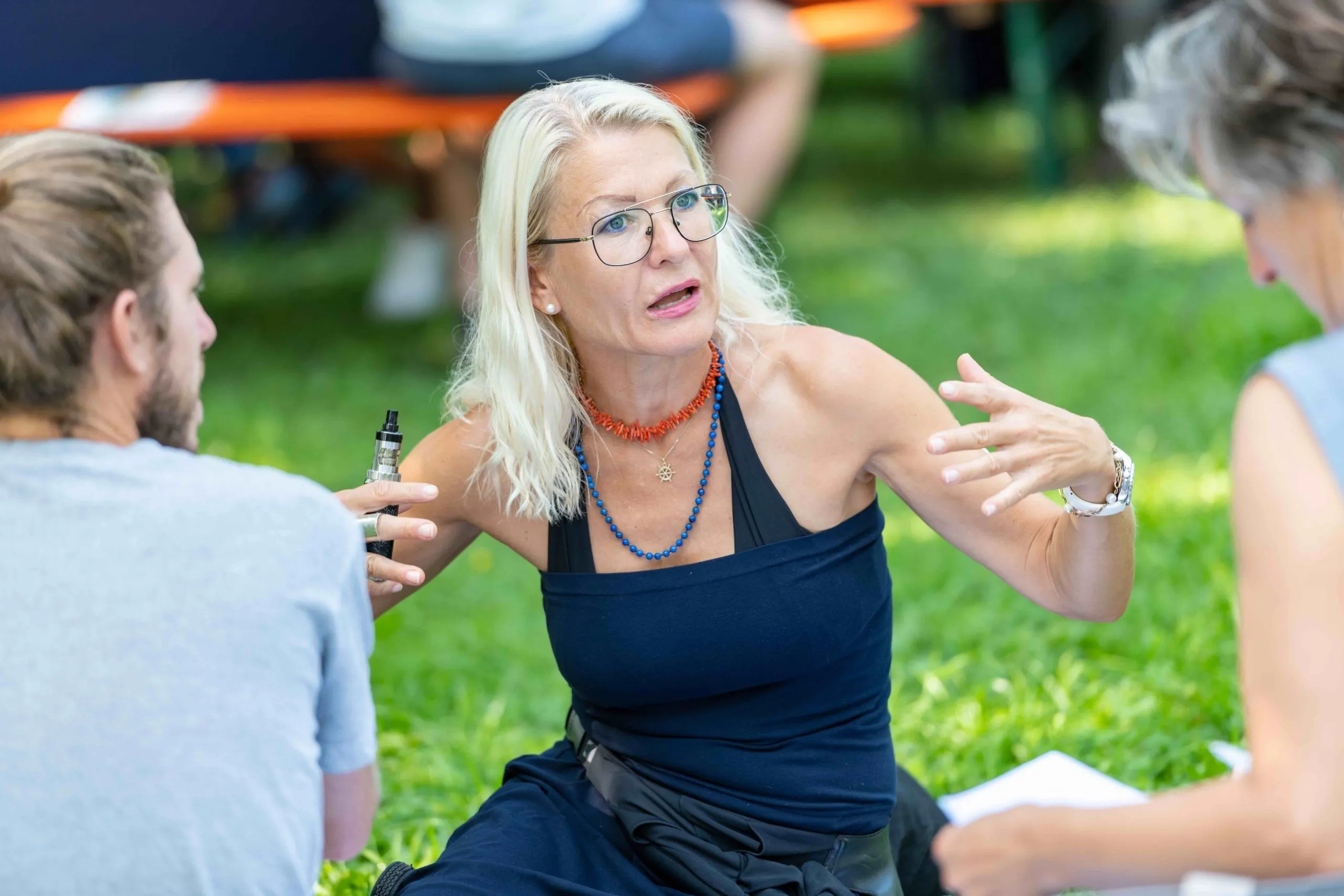 Frau sitzend in einer Wiese und 2 Männer im Hintergrund