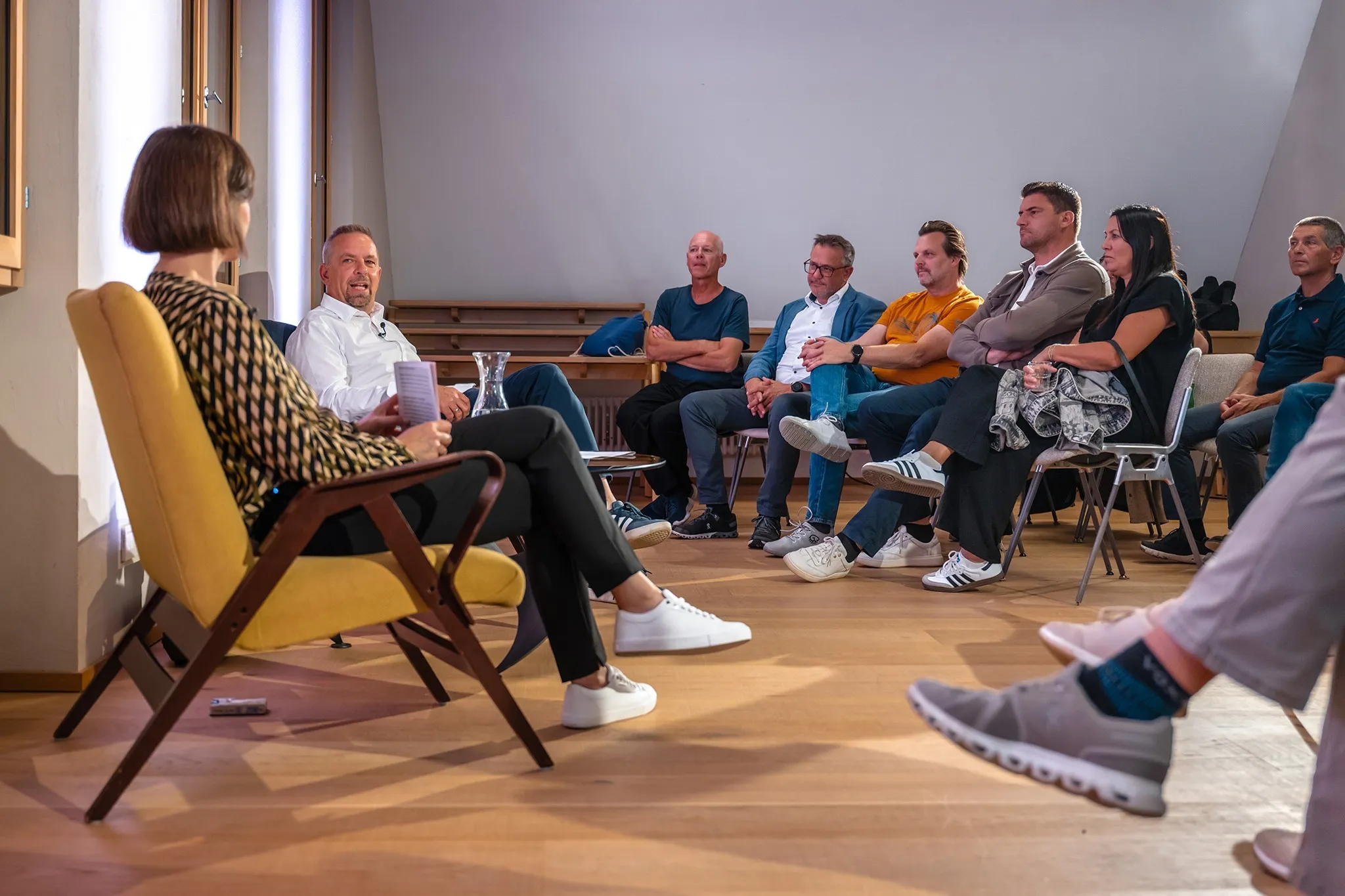 Publikum und Moderatorin Carmen Jurkovic-Burtscher hört gespannt zu während Oliver Loacker von seinem Arbeitsleben berichtet.