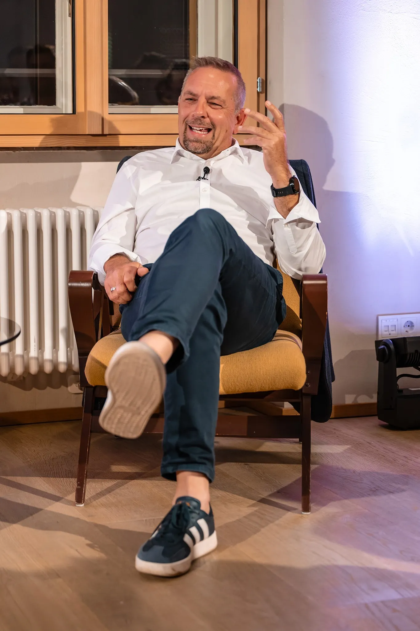 Oliver Loacker erzählt von seinem Arbeitsleben. Sitzt mit verschränkten Beinen bemütlich auf einem Sessel.