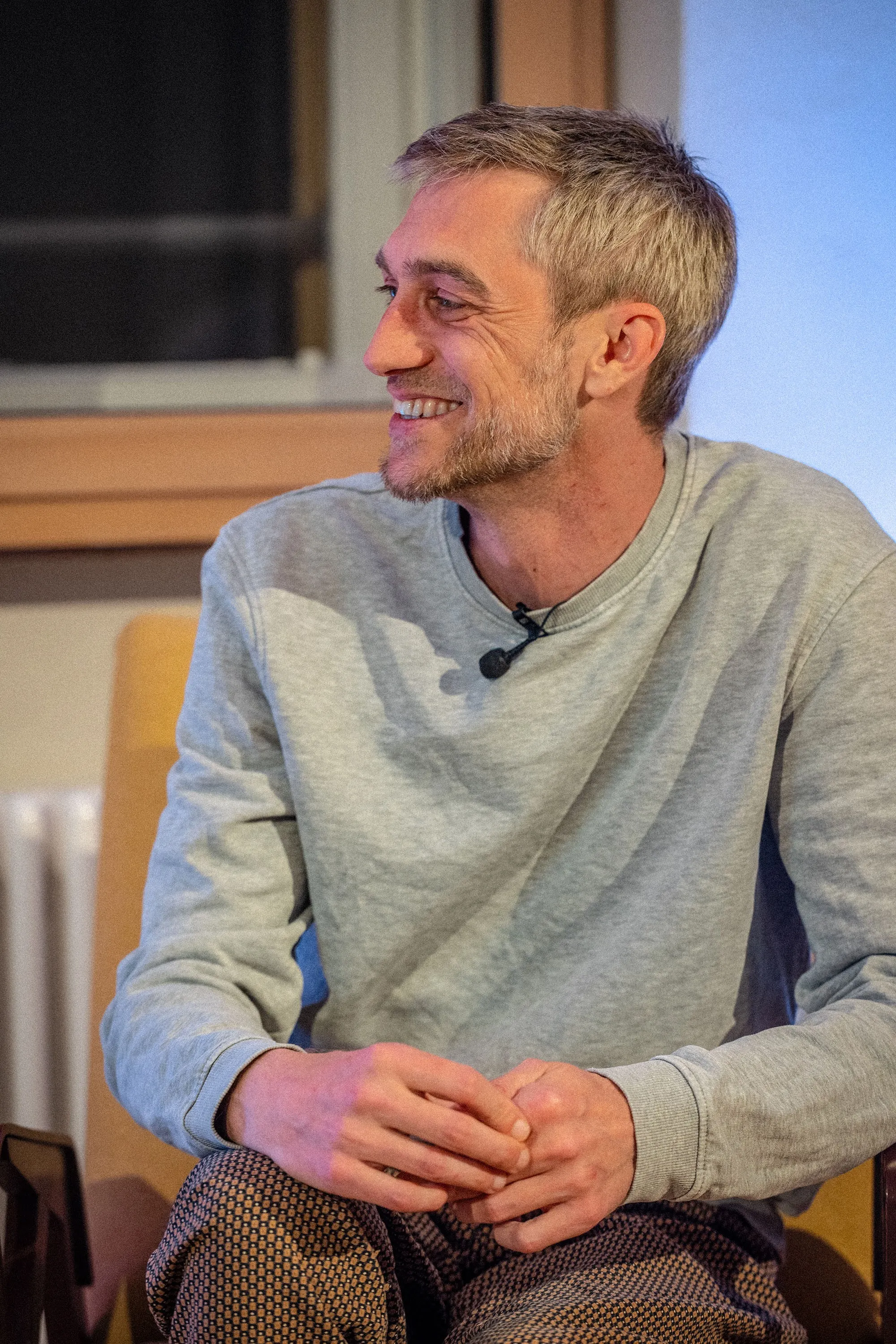 Philipp Böhler (MC Pille One) sitzt bei einer Veranstaltung der ArbeitsLebensGeschichten in der Schaffarei der AK Vorarlberg in Feldkirch auf einem Stuhl und spricht mit einer Moderatorin. Beide sind einander zugewandt, zwischen ihnen steht ein kleiner Tisch mit Wasserflaschen. Die Atmosphäre wirkt ruhig und aufmerksam, der Raum ist modern und warm beleuchtet.