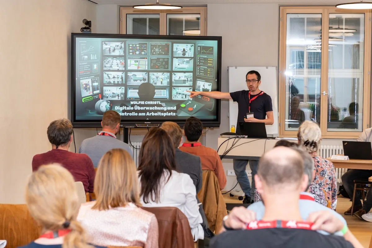 Vortragender auf einen großen Bildschirm zeigend mit Publikum im Vordergrund