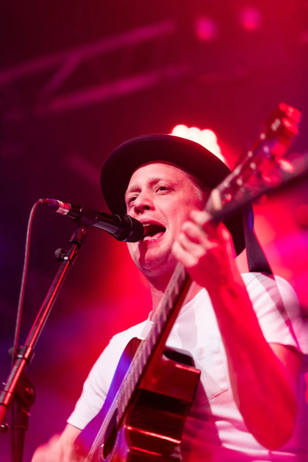 Sänger mit Hut und Gitarre auf der Schaffarei Bühne mit rotem Hintergrund