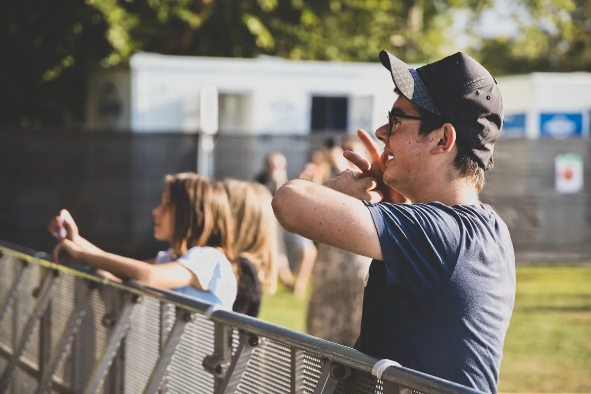 Mann mit Baseballcap und blauem T-Shirt vor einer Bühnen Absperrung