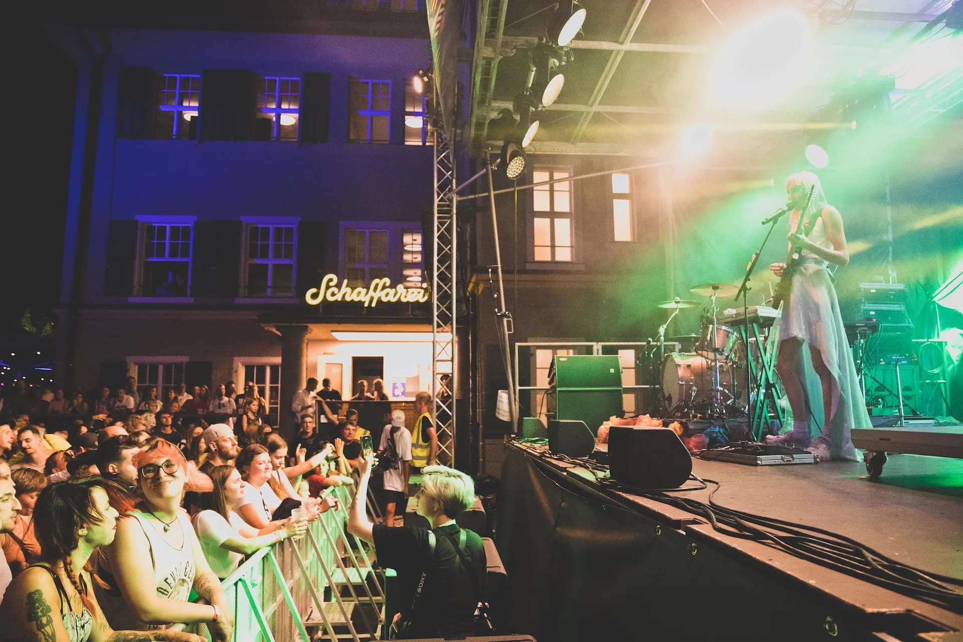 Frau Gitarre spielend auf der Bühne und Publikum vor der Schaffarei Bühne
