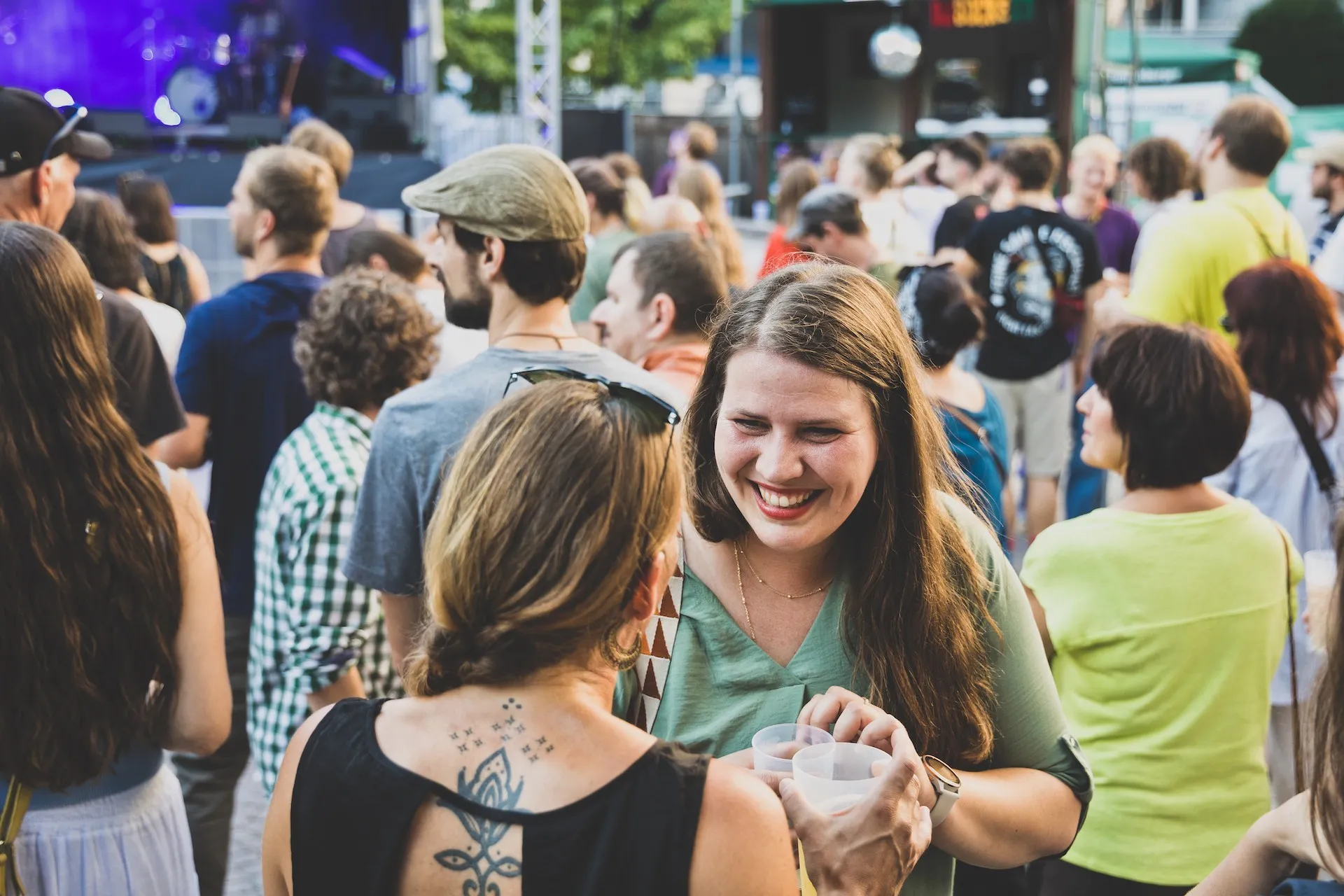 Lachende Frau in grünem Oberteil unterhält sich und im Hintergrund eine Menschenmenge