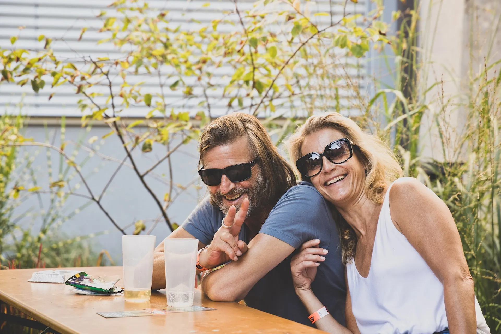 Zwei lachende sitzende Personen mit Sonnenbrille und Getränken
