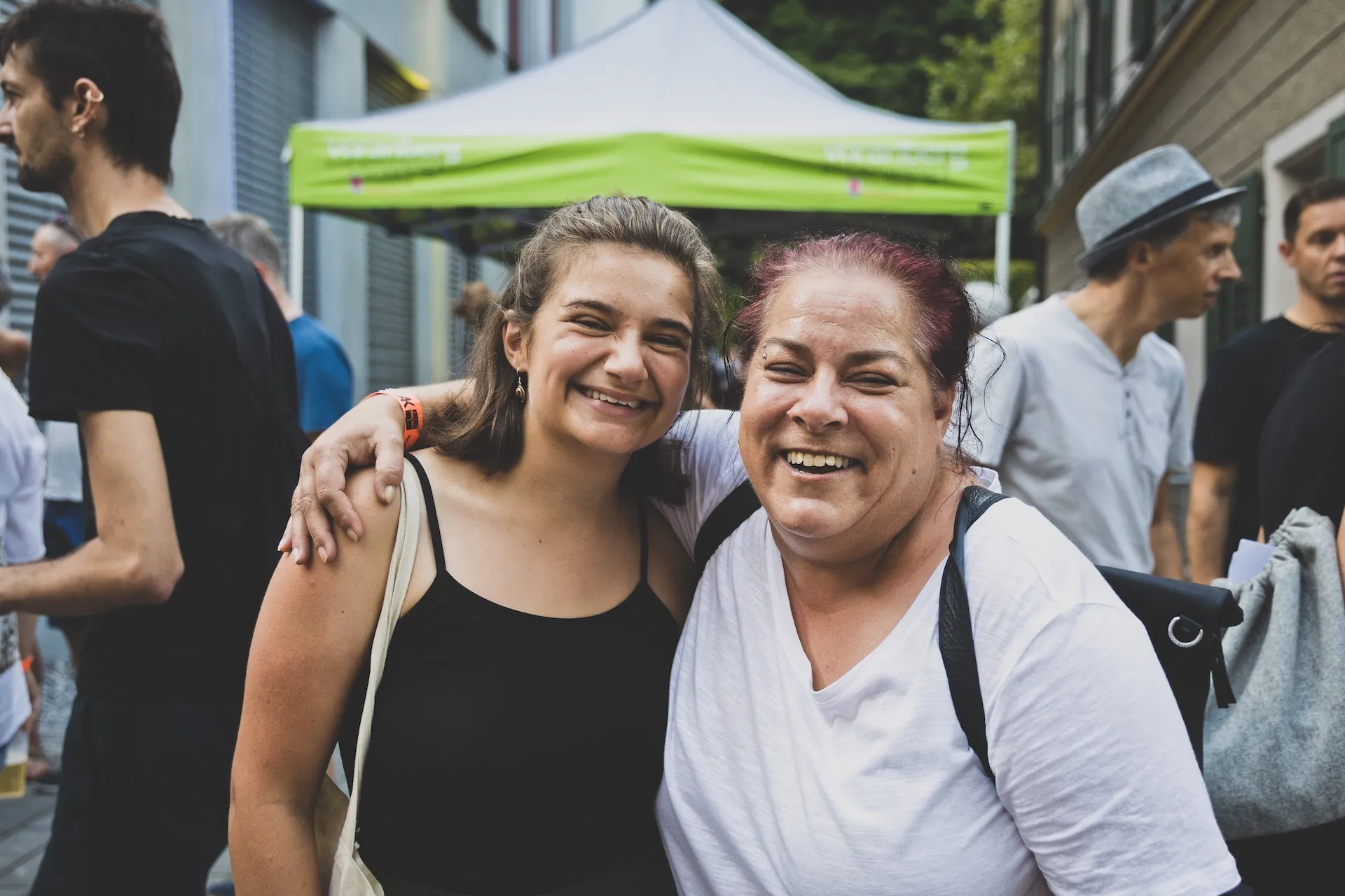 Zwei lachende Frauen umarmen sich im Hintergrund eine paar Menschen