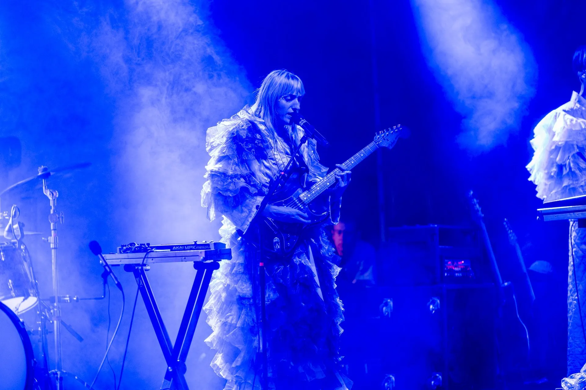 Sängerin mit Gitarre und großem Mantel mit blauem Hintergrund auf der Schaffarei Bühne