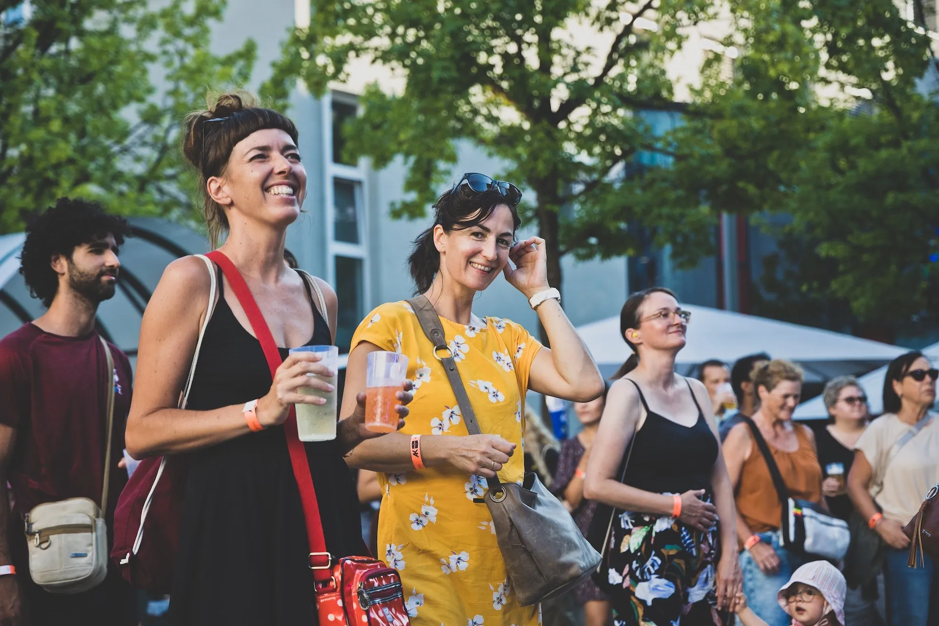 Menschenmenge lachend, halten Getränke und hören Musik in entspannter Atmosphäre.