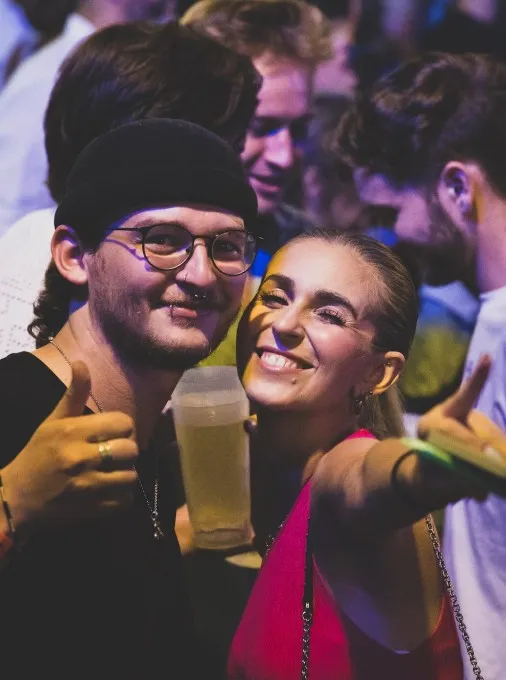 Zwei lächelnde Personen mit Daumen nach oben zeigend und Getränke in der Hand