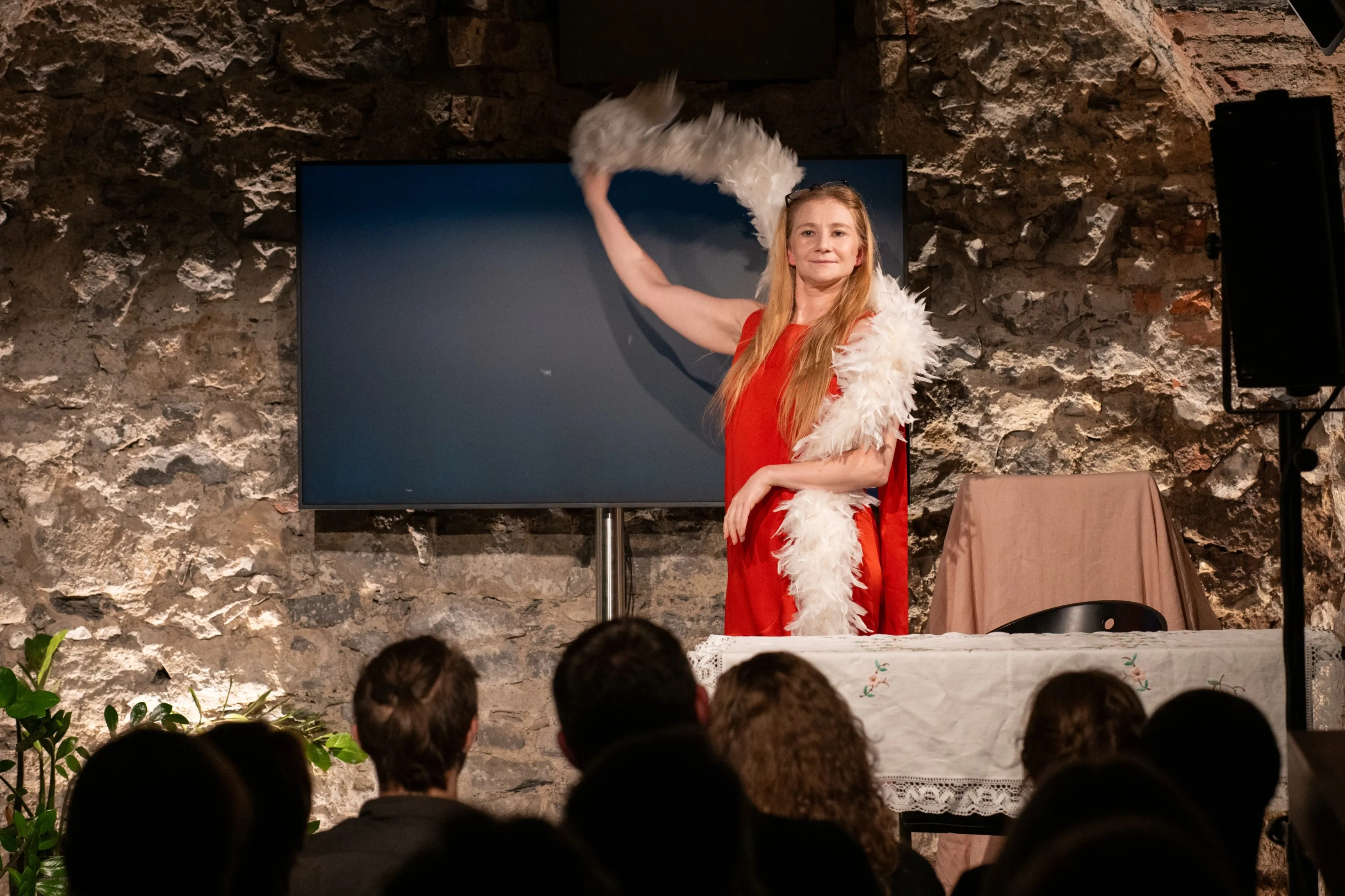 Schauspielerin Vivien Causemann in einem roten Kleid schwingt eine weiße Federboa auf einer Theaterbühne im Stück „Schöne alte Arbeitswelt“.