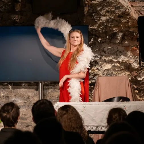 Schauspielerin Vivien Causemann in einem roten Kleid schwingt eine weiße Federboa auf einer Theaterbühne im Stück „Schöne alte Arbeitswelt“.