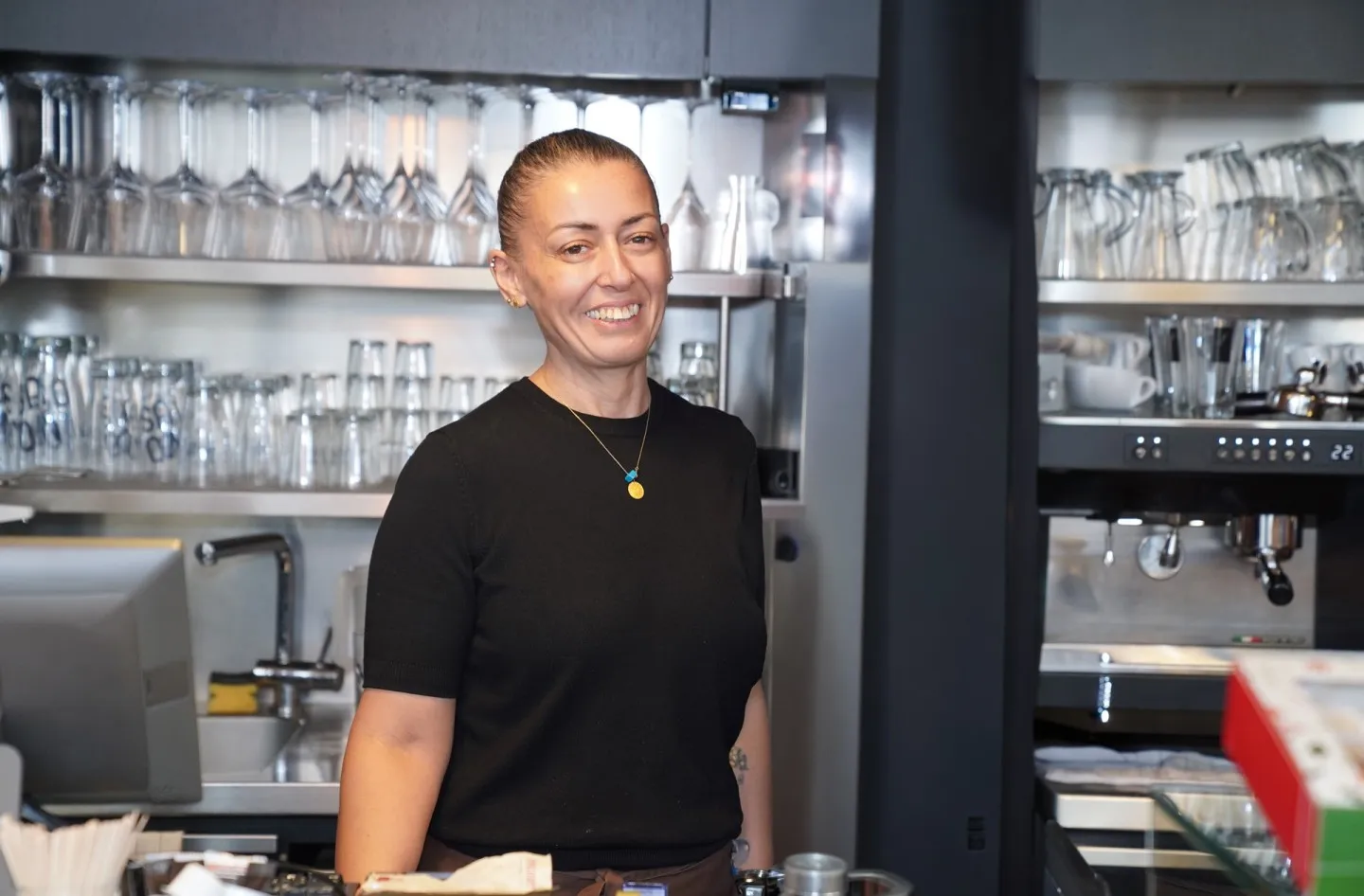 Sükran Keles bei der Arbeit im Café hinter der Theke, lacht in die Kamera.