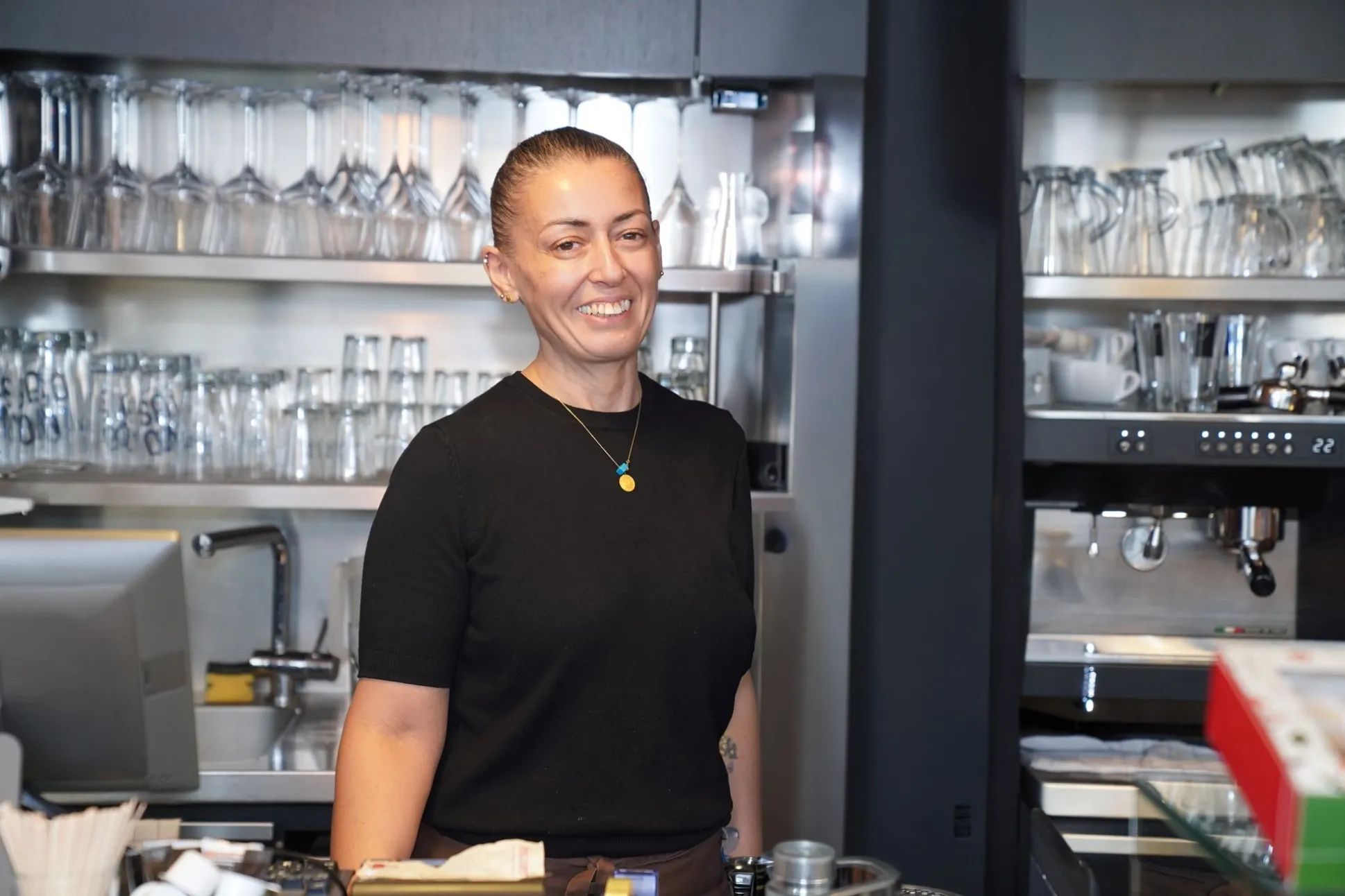 Sükran Keles bei der Arbeit im Café hinter der Theke, lacht in die Kamera.
