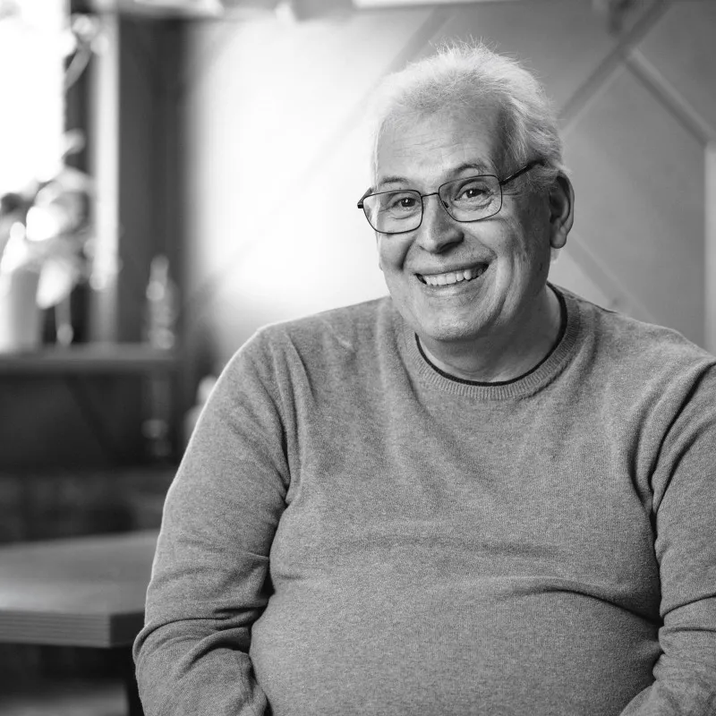 Lächelnder älterer Mann mit Brille in grauem Pullover, Schwarz-Weiß-Porträt.