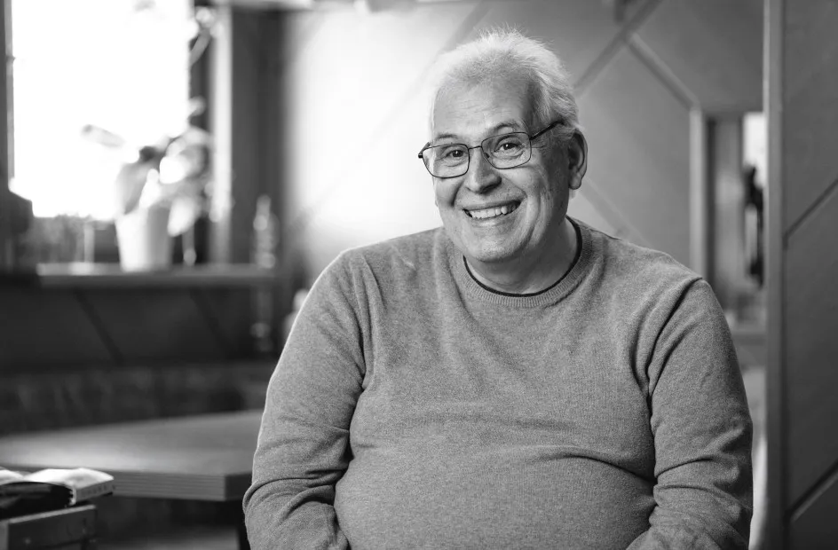 Lächelnder älterer Mann mit Brille in grauem Pullover, Schwarz-Weiß-Porträt.